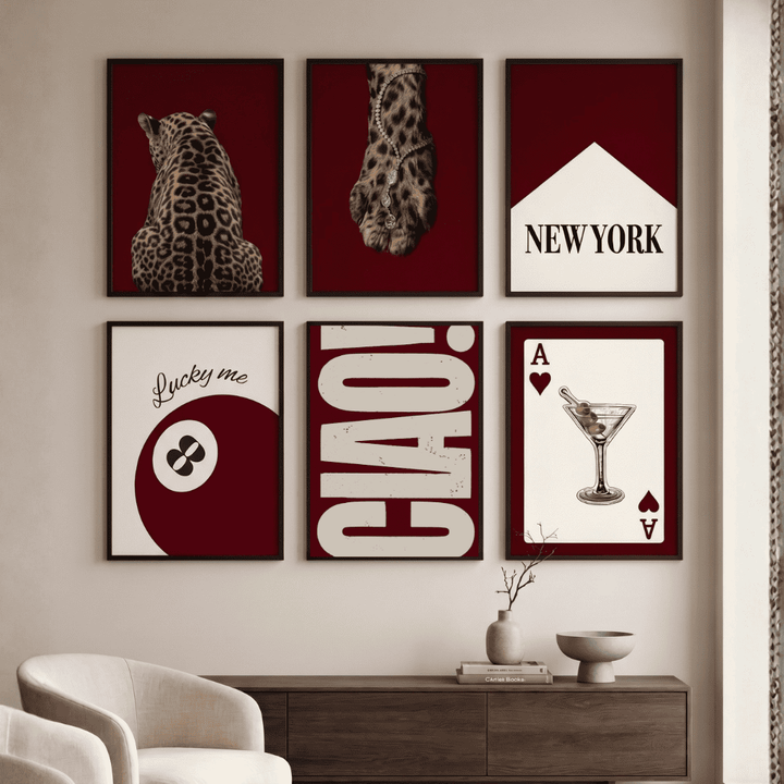 Six framed wall art prints arranged in a 2x3 grid on a beige wall above a dark wood console. The prints feature deep burgundy and white designs including a leopard, a glove, the word NEW YORK, a yin-yang with 'Lucky me', large 'CIAO!' lettering, and an Ace of Hearts martini card.